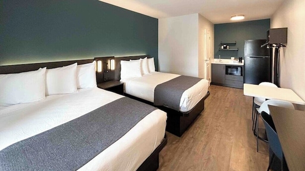 Une chambre d’hôtel avec deux lits, un bureau, une chaise, une kitchenette et un téléviseur.