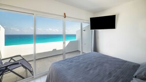 A bedroom with a bed, a TV, and a balcony with a view of the ocean. - Relax by the Beach - 3 Bedrooms 2408 (Cancún)