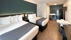 Une chambre d’hôtel avec deux lits, un bureau, une chaise, une kitchenette et un téléviseur.
