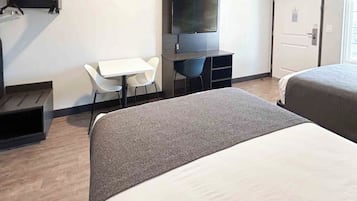A hotel room with a bed, a desk with a chair, a TV mounted on the wall, and a door.