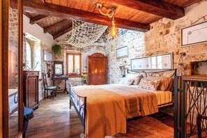 A rustic bedroom with a stone wall, wooden beams, a bed with a patterned bedspread, a desk with a chair, and a hanging light fixture. - Traditional apt in stone house in heart of Trogir (Trogir)