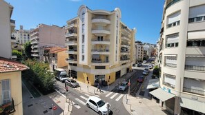 Un immeuble à plusieurs étages doté de balcons, un passage piéton et des voitures garées.