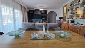 Ein Essbereich mit einem Holztisch, zwei Glaswindlichtern und einer Couch im Hintergrund.