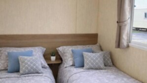 Une chambre avec deux lits, une table de chevet ornée d’une plante et une fenêtre avec des rideaux.