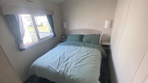 Una habitación pequeña con cama individual, ventana, mesita de noche y tocador.