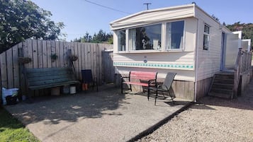 Une maison mobile dotée d’un patio, d’une table, de chaises et d’une voiture garée à proximité.