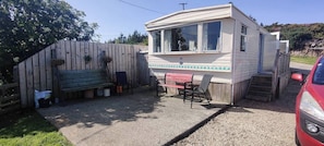 A mobile home with a patio area, a table, chairs, and a car parked nearby.