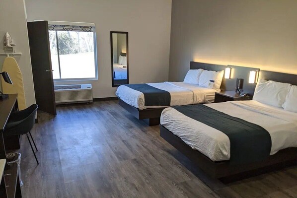 Una camera d'albergo con due letti, una scrivania, una sedia, uno specchio e una finestra.