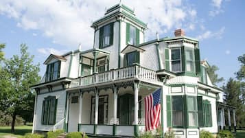 A large, white building with green trim and multiple windows, featuring a balcony and an American flag.