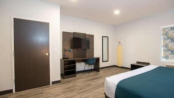 A hotel room with a bed, a desk with a chair, a television, and a window with a geometric pattern.