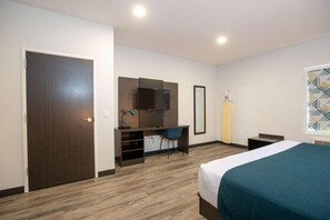 Una camera d'albergo con un letto, una scrivania con una sedia, una televisione e una finestra con motivo geometrico.