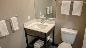 Un bagno con un lavandino bianco, uno specchio e un water. Asciugamani appesi a un porta-asciugamani e uno scaffale con asciugamani piegati.