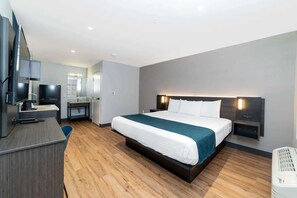 A modern hotel room with a bed, desk, TV, and a mirror.
