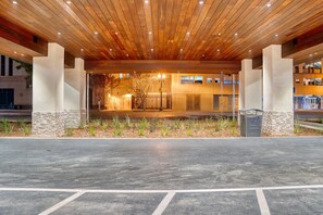 A building entrance with a wooden ceiling, stone pillars, and a paved area in front.