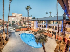 A hotel with a swimming pool, palm trees, and a view of a cityscape.