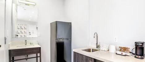 Una cocina compacta equipada con refrigerador, lavamanos, microondas y cafetera.