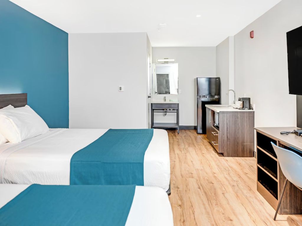 Habitación de hotel con dos camas, un escritorio, un televisor y un espejo.
