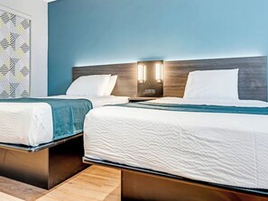 A hotel room with two beds, a wooden headboard, and a wall-mounted light fixture.