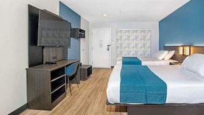 Habitación de hotel con una cama, un escritorio con silla, un televisor y una puerta que da a otra habitación.