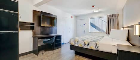 A modern hotel room with a bed, desk, and wardrobe.