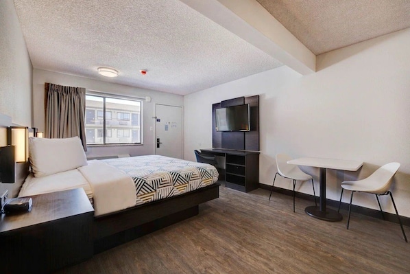 A hotel room with a bed, desk, TV, and two chairs.