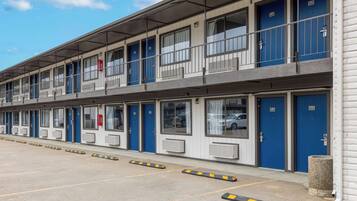 Un motel de varios pisos con puertas azules, habitaciones numeradas y un estacionamiento cubierto.