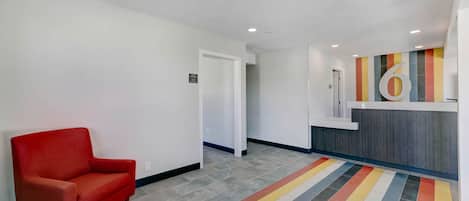 A hotel lobby with a red armchair, a reception desk, and a colorful striped carpet.