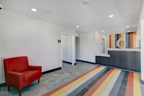 Un hall d’hôtel avec un fauteuil rouge, un comptoir d’accueil et un tapis rayé aux couleurs vives.