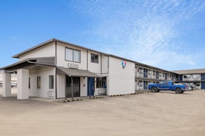 Un motel composé d’un bâtiment d’un seul étage, doté d’une entrée abritée et d’un espace de stationnement où se trouve un camion bleu.