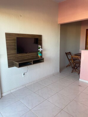 A living room with a flat-screen TV mounted on a wooden panel, a small table with chairs, and a tiled floor. - LM Flats - Beach, Pool and Exclusivity for 20 (Aquiraz)