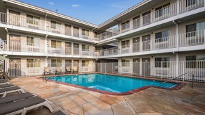 A multi-story hotel with a central swimming pool, balconies, and a patio area with lounge chairs.