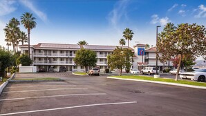 A multi-story hotel with a parking lot, palm trees, and a clear sky.