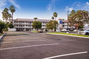 A multi-story hotel with a parking lot, palm trees, and a clear sky.