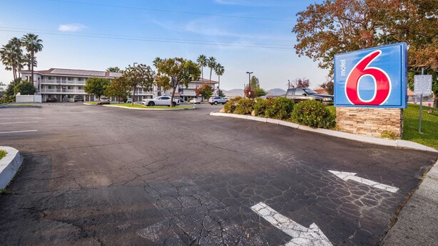 A motel sign with the number 6, a parking lot with directional arrows, and a building with multiple stories in the background.