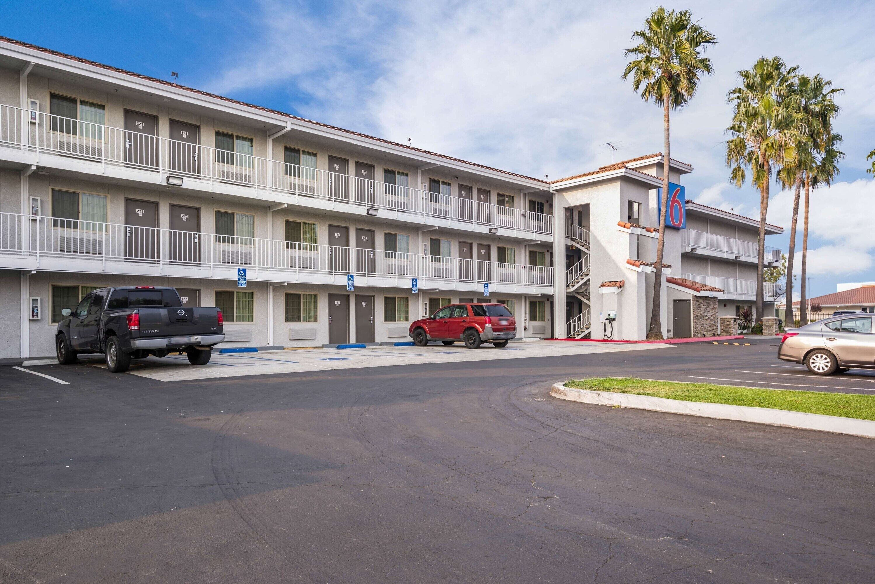A motel with a two-story structure, a parking lot, and a few vehicles.
