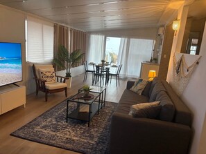 Ein Wohnzimmer mit Sofa, Sessel, Couchtisch und Fernseher. Es gibt einen Essbereich mit Tisch und Stühlen.