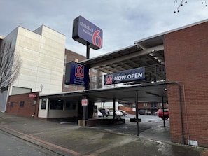 A hotel entrance with a sign indicating 'Studio Suites 6' and 'NOW OPEN'.