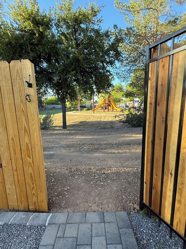 Una verja de madera que da acceso a un parque infantil con tobogán y estructuras para escalar.