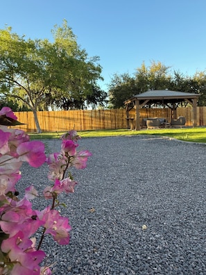 A patio area with a gravel surface, a wooden fence, and a wooden gazebo with seating. - Unique 3-bedroom house in beautiful Chandler with cool AC comfort, huge backyard (Chandler)