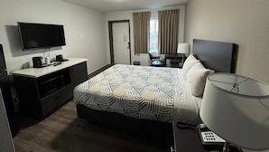 A hotel room with a bed, a desk, a television, a lamp, and a window with curtains. - Smart Choice for Budget-Conscious Travelers Near Dinings | City Sandwich -0.1 mi (Clark County)