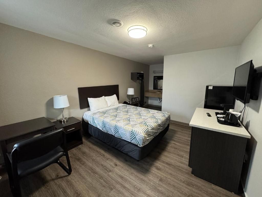 Hotellihuone, jossa on sänky, työpöytä, tuoli, televisio ja pieni keittotila.
