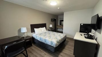 A hotel room with a bed, desk, chair, TV, and a kitchenette area.