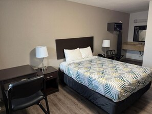 Une chambre d’hôtel comprenant un lit, un bureau, une chaise, une table de chevet, une lampe, un téléviseur et un miroir.