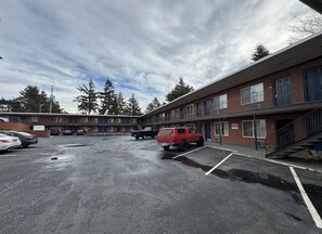 Ein mehrstöckiges Motel mit Parkplatz, auf dem ein rotes Fahrzeug geparkt ist, und einer Treppe, die zum Eingang führt.