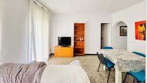 Una habitación con dos camas, un televisor sobre un tocador de madera, una mesa con sillas y una puerta que da a otra habitación.