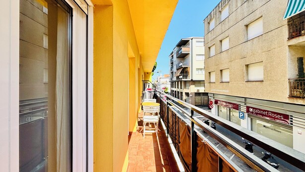 Un balcón estrecho con toldo amarillo, vista de edificios vecinos y un cartel que dice 'Cabinet Roses' a la derecha.