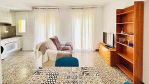 Un espacio habitable compacto con kitchenette, un sofá, un televisor y una estantería de madera.