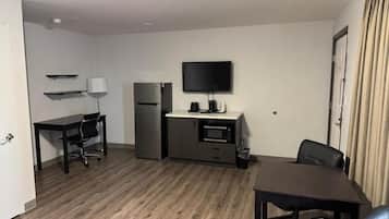 Una habitación compacta con kitchenette, una televisión de pantalla plana, una mesa de comedor con sillas y una puerta con cortinas.