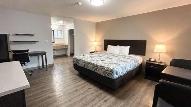 Quarto de hotel com cama, escrivaninha, cadeira e uma pequena cozinha.