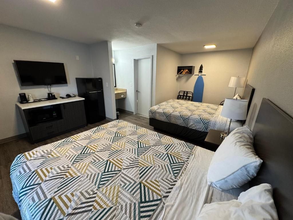 Une chambre d’hôtel avec un grand lit, un lit plus petit, un bureau avec un téléviseur à écran plat, un réfrigérateur, une chaise et une lampe.